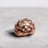bague tressee vermeil vue dessus | 26 Passage, Créatrice de bijoux à Paris Copper-toned woven ball sculpture resting on a gray speckled floor.