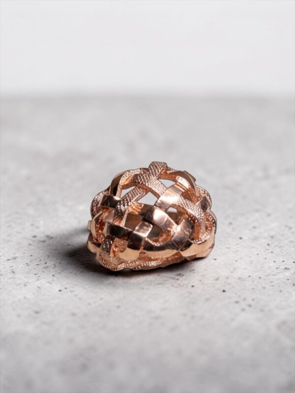 bague tressee vermeil vue dessus | 26 Passage, Créatrice de bijoux à Paris Copper-toned woven ball sculpture resting on a gray speckled floor.