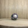 bague marie antoinette argent noir peridots ligne saphirs rose et perle eau douce creme vue de face | 26 Passage, Créatrice de bijoux à Paris Silver ring with a large central pearl surrounded by a pink gemstone halo, resting on a wooden surface.