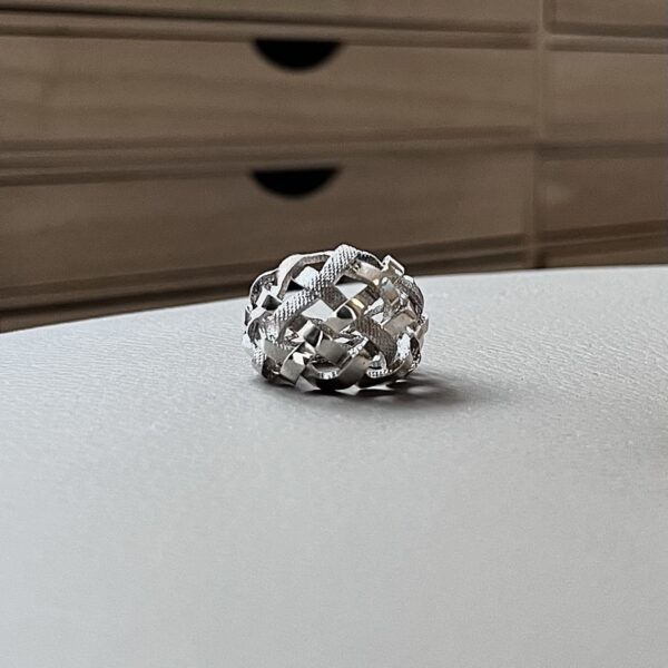 bague tressee argent vue de face | 26 Passage, Créatrice de bijoux à Paris Close-up of a silver braided ring resting on a pale desk, with a brown filing cabinet blurred in the background.