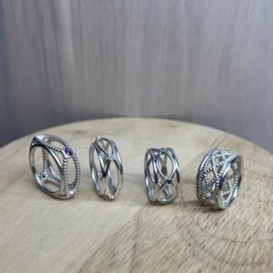 groupe collection bagues filaires collection femme Set of four silver rings with intertwining bands and small gemstones on a wooden surface, showcasing varied designs.