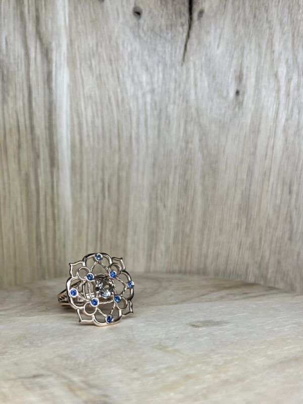 Bague Princesse en vermeil quartz fume saphirs bleus collection les pierres | 26 Passage, Créatrice de bijoux à Paris Silver flower-ring with blue gemstone accents resting on light wood surface.