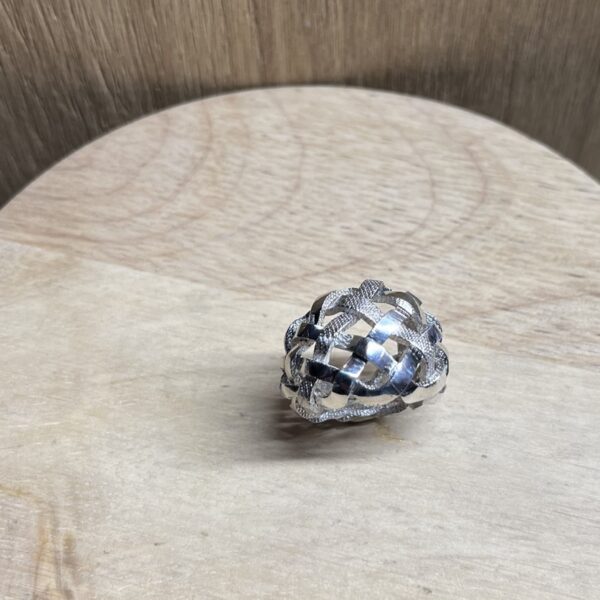 bague tressee argent vue dessus | 26 Passage, Créatrice de bijoux à Paris Close-up of a silver woven bead/ring resting on a light wood table.