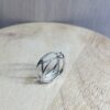 bague filaire carree arrondi saphir parme collection femme | 26 Passage, Créatrice de bijoux à Paris Silver geometric ring with interconnected bands and a small gemstone, resting on a light wooden surface.