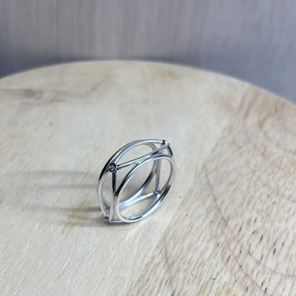 bague filaire carree arrondi saphir parme collection femme | 26 Passage, Créatrice de bijoux à Paris Silver geometric ring with interconnected bands and a small gemstone, resting on a light wooden surface.