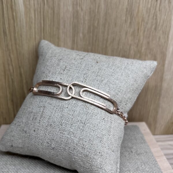 bracelet double trombone vermeil a plat sur coussin | 26 Passage, Créatrice de bijoux à Paris Rose gold bracelet with two elongated rectangular links resting on a light gray cushion.