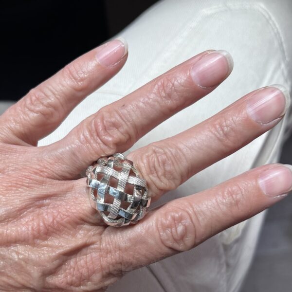 bague tressee argent vue dessus portee | 26 Passage, Créatrice de bijoux à Paris Close-up of a hand wearing a large interwoven silver ring on the finger, with light pink nails.