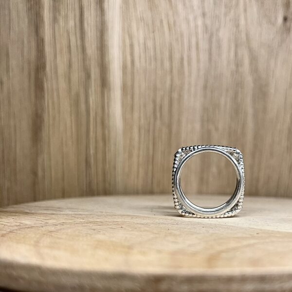 bague filaire carree arondie perlee grenat rhodolite collection femme vue profil | 26 Passage, Créatrice de bijoux à Paris Close-up of a silver beaded square ring on a wooden surface.