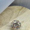Bague Princesse en vermeil quartz fume saphirs bleus collection les pierres vue dessus | 26 Passage, Créatrice de bijoux à Paris Intricate flower-shaped ring with blue stones at the petal edges and a central gray gemstone on a light surface.