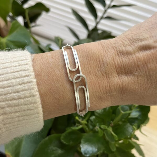 bracelet double trombone argent porte 2 | 26 Passage, Créatrice de bijoux à Paris Silver bracelet with large rectangular links on a wrist against a leafy background.