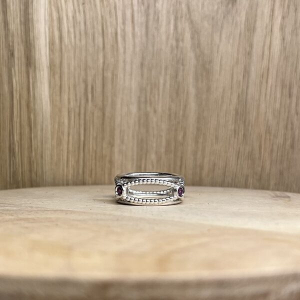 bague filaire carree arondie perlee grenat rhodolite collection femme | 26 Passage, Créatrice de bijoux à Paris Silver beaded ring with two small purple stones, placed on a light wood surface.