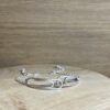 bracelet double trombone argent a plat | 26 Passage, Créatrice de bijoux à Paris Silver bracelet with interlocking rectangular links resting on a light wooden surface, sparkly finish visible at edges.