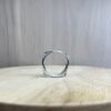 bague filaire carree arrondi saphir parme collection femme vue cote | 26 Passage, Créatrice de bijoux à Paris Close-up of a hollow silver ring setting standing on a light wooden tabletop with a blurred gray background.