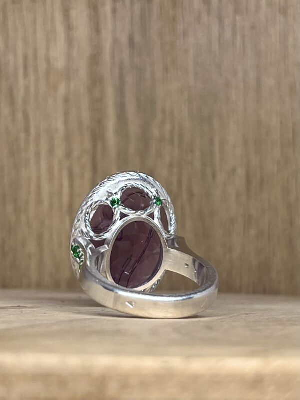 IMG_4280 | 26 Passage, Créatrice de bijoux à Paris Close-up of a silver ring with a purple gemstone and green accents on a wooden surface.