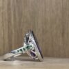 IMG_4282 | 26 Passage, Créatrice de bijoux à Paris Close-up of a silver braided ring with green gemstones on a wooden surface