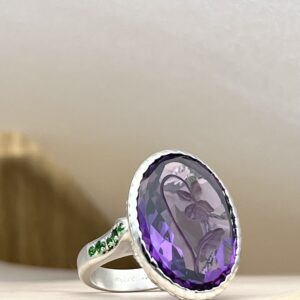 IMG_4283 Silver ring with a large faceted purple gem as the centerpiece, resting on a light surface.