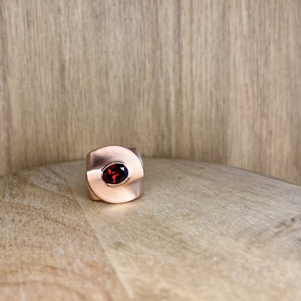 Bague twist vermeil grenat vue trois quart collection femme les pierres | 26 Passage, Créatrice de bijoux à Paris Close-up of a light brown wood floor with a pink curved object and a red gem peeking into the bottom edge of the frame.