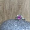 Bague mini princesse argent tourmaline rose grenats tsavorite | 26 Passage, Créatrice de bijoux à Paris Silver ring with a pink gemstone centerpiece, accented by small green stones, resting on a gray rock with a wooden background.