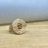 bague meringue vermeil diamants bruns vue trois quart | 26 Passage, Créatrice de bijoux à Paris Gold ring with concentric circular design and diamond-studded bands, resting on a wooden surface in soft light.