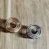 bague meringue vermeil et argent vue dessus | 26 Passage, Créatrice de bijoux à Paris Two circular rings with intertwined inner loops, one rose gold with clear stones and one silver with purple stones, on a wooden surface.