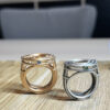 bague meringue vermeil vue cote | 26 Passage, Créatrice de bijoux à Paris Rose gold ring with blue gem and intricate openwork beside a silver ring with green gem on a wooden surface.