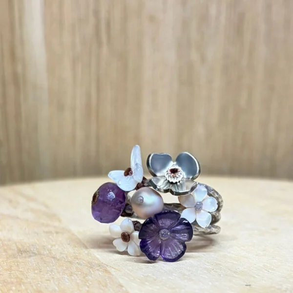 bague prairie argent amethyste nacre rose perle | 26 Passage, Créatrice de bijoux à Paris Flower-themed multi-band ring with purple and white petal charms on a wooden surface, jewelry detail jewelry.