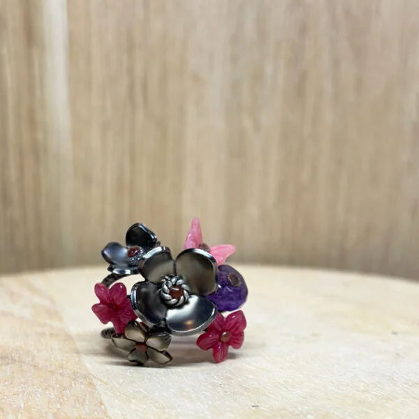 bague prairie argent noir agate teintee rose amethyste nacre grise | 26 Passage, Créatrice de bijoux à Paris Cluster of metal flower charms in black, pink, and purple on a wooden surface