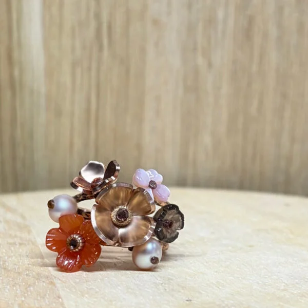 bague prairie vermeil nacre perle fleur quartz fume fleur cornaline | 26 Passage, Créatrice de bijoux à Paris Cluster ring with metal flower petals in copper and pink tones, set with small beads on a wooden surface.
