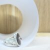 chevaliere nacre saphir sonkia vue profil | 26 Passage, Créatrice de bijoux à Paris Close-up of a white paper plate on a wooden surface with a silver decorative heel-shaped jewelry piece resting on its edge.