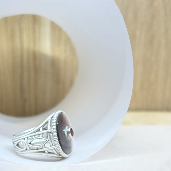 chevaliere nacre saphir sonkia vue profil | 26 Passage, Créatrice de bijoux à Paris Close-up of a white paper plate on a wooden surface with a silver decorative heel-shaped jewelry piece resting on its edge.