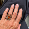 bague double branche melange vermeil argent noir citrine madère | 26 Passage, Créatrice de bijoux à Paris Close-up of a hand wearing a bronze-toned ring with an orange gemstone, set in a thorny, nest-like metal design on the ring finger