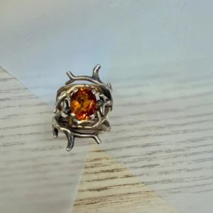 Silver-toned ring with a tangled branch setting and an oval orange gem at center.