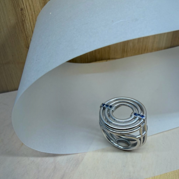 bague meringue argent saphirs bleus | 26 Passage, Créatrice de bijoux à Paris Silver multi-band ring with blue stones resting on a curved white backdrop.