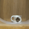 bague trombone argent quartz fume ovale vue face | 26 Passage, Créatrice de bijoux à Paris Silver ring with an oval smoky quartz gemstone set in a geometric open frame, resting on a light wood surface.