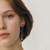 boucles tourmaline poire quartz fume cristal de roche sur argent portees | 26 Passage, Créatrice de bijoux à Paris Close-up of a woman's left face showcasing long multi-chain earrings with purple gemstone and a teardrop pendant.