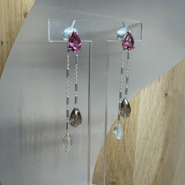 boucles tourmaline poire quartz fume cristal de roche sur argent vue trois quart | 26 Passage, Créatrice de bijoux à Paris Silver drop earrings with pink teardrop gems and dangling chains displayed on a metal stand.