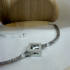 bracelet mikado argent zircon a plat | 26 Passage, Créatrice de bijoux à Paris Silver-toned multi-strand bracelet with a square metallic pendant featuring a small diamond-shaped cutout, displayed on a white surface with a wooden display in the background.