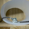 bracelet mikado argent zircon vue de face | 26 Passage, Créatrice de bijoux à Paris Square silver pendant necklace with a diamond centerpiece on a braided chain, resting on a white curved prop behind it.