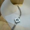 bracelet mikado argent zircon vue de haut | 26 Passage, Créatrice de bijoux à Paris Silver multi-strand necklace with a square pendant featuring a central gemstone on a curved white display board.