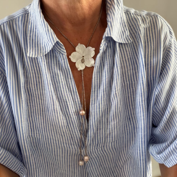 Close-up of a blue striped shirt with a white flower pendant necklace and pearl-dropped chain.