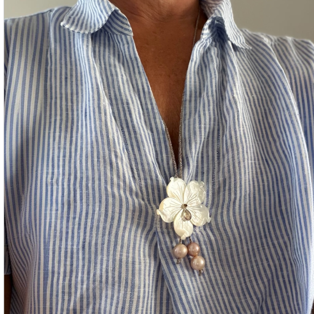 Close-up of a blue striped blouse with a white flower pin at the neckline, featuring three pearl drops.