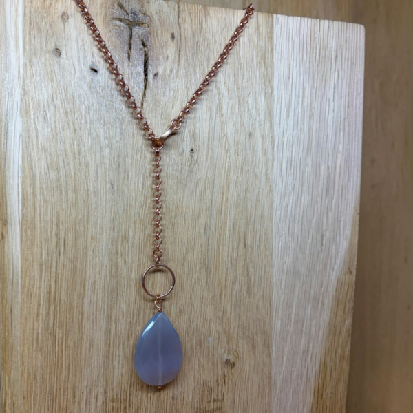 Rose‑gold chain necklace with a blue teardrop pendant hanging from a circular ring, set against a wooden background.