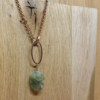 Copper chain necklace with an oval green gemstone pendant hanging from a wooden surface.