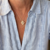 collier mikado vermeil zircon sur chaine porte | 26 Passage, Créatrice de bijoux à Paris Gold square-frame pendant with a small diamond centered on a thin chain resting on a blue-and-white striped shirt neckline