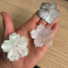 Hand holding four carved flower-shaped resin buttons in pearly white and iridescent finishes on the palm of a hand.